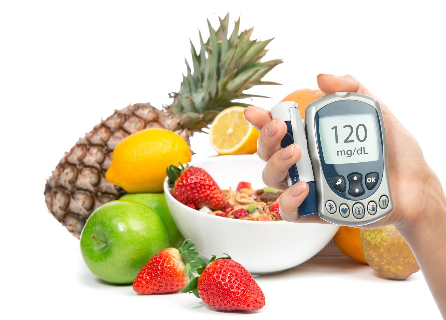 A colorful array of fruits such as lemon, pineapple, and strawberries. In the foreground, a hand holds a glucose monitor