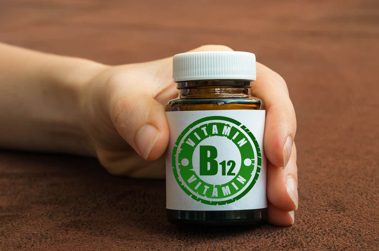 Human hand holding a bottle of pills with vitamin B12 supplements