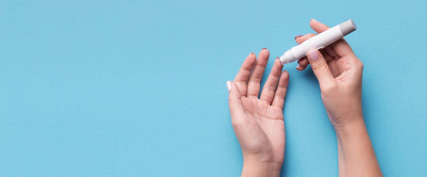 Two hands shown against a blue background as the persons pricks their finger so they can test their blood sugar