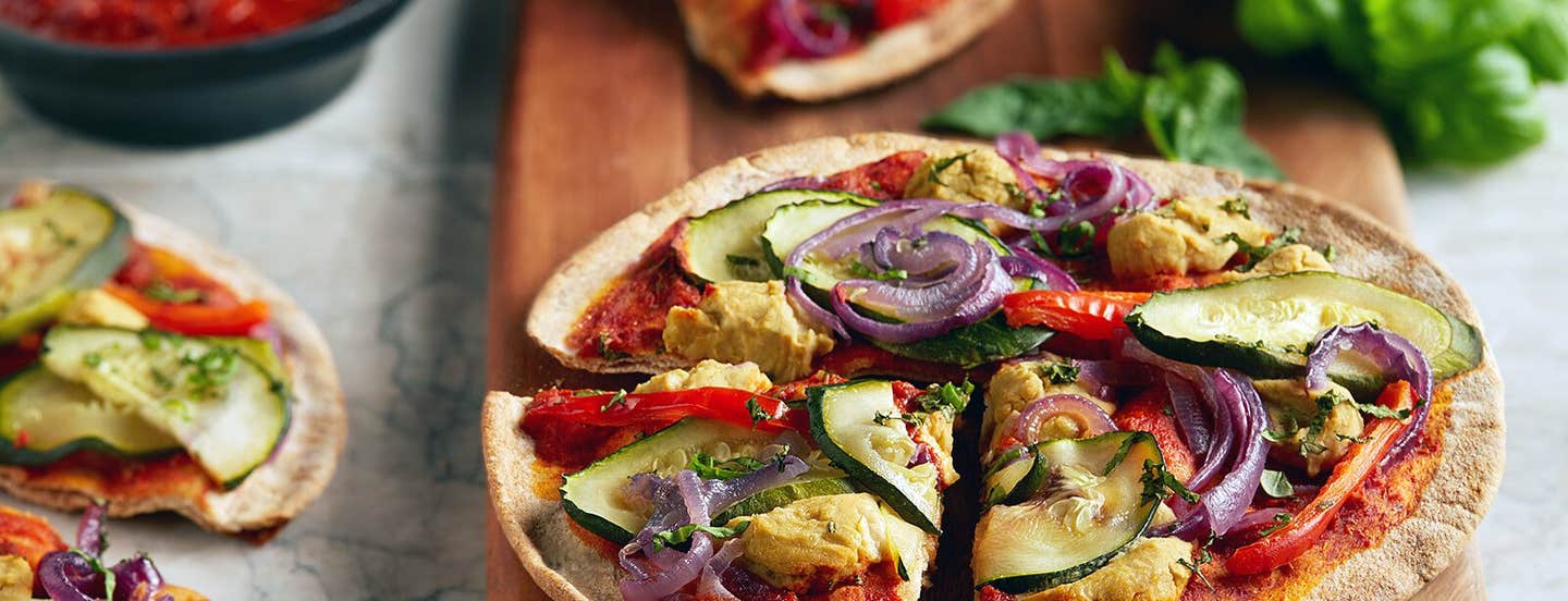 Cheesy Vegan Veggie Pizzette cut into quarters on a wooden chopping board, with other pizzettes in the background