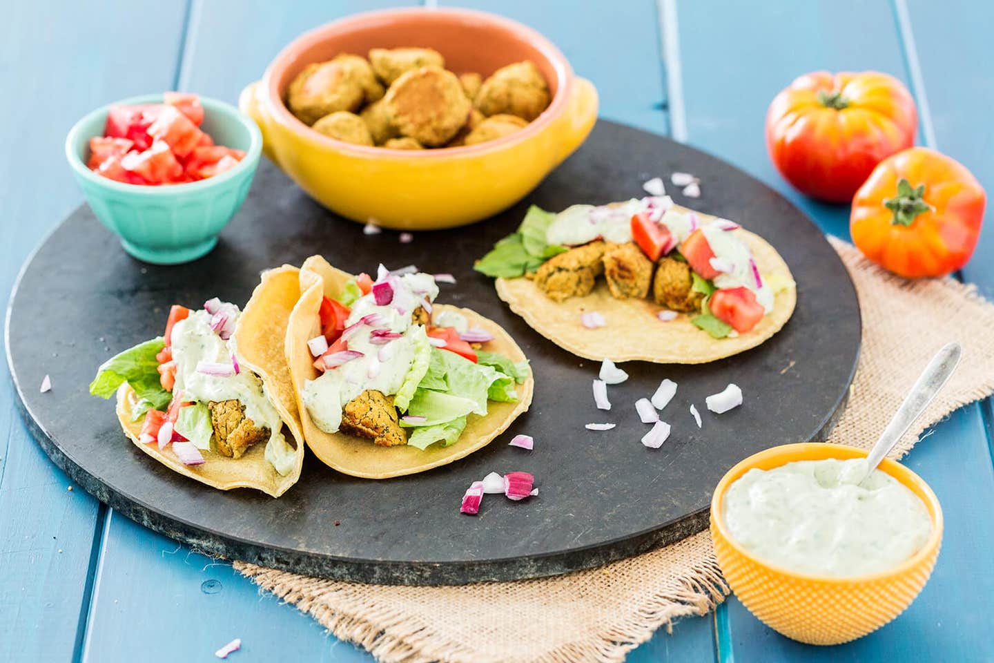 A round black baking tray with three tacos and a bowl of falafel