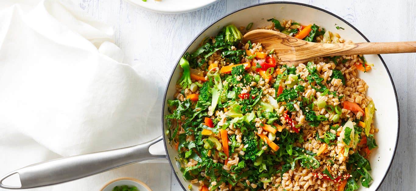 Oil-Free Farro Fried Rice in a white skillet with a wooden serving spoon