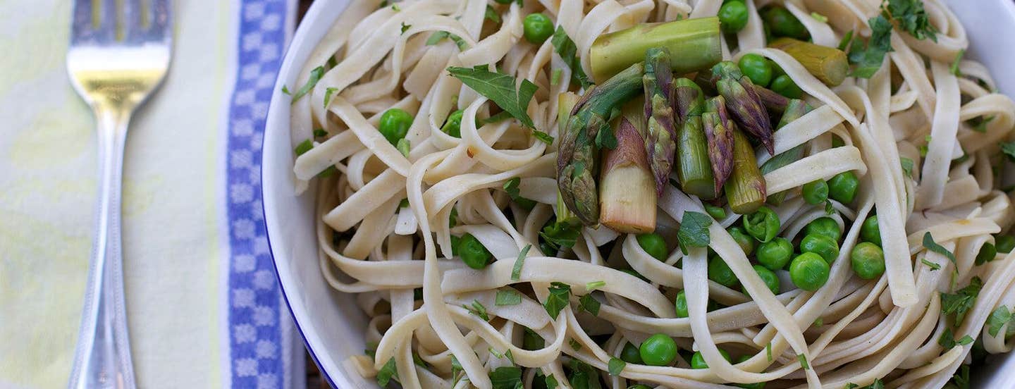 Fettuccine with Grilled Asparagus, Peas, and Lemon in a white bowl with a fork to one side