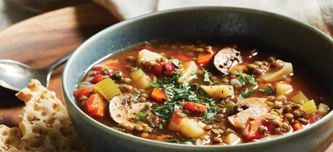 French Green Lentil Stew in a blue ceramic bowl with a side of crackers