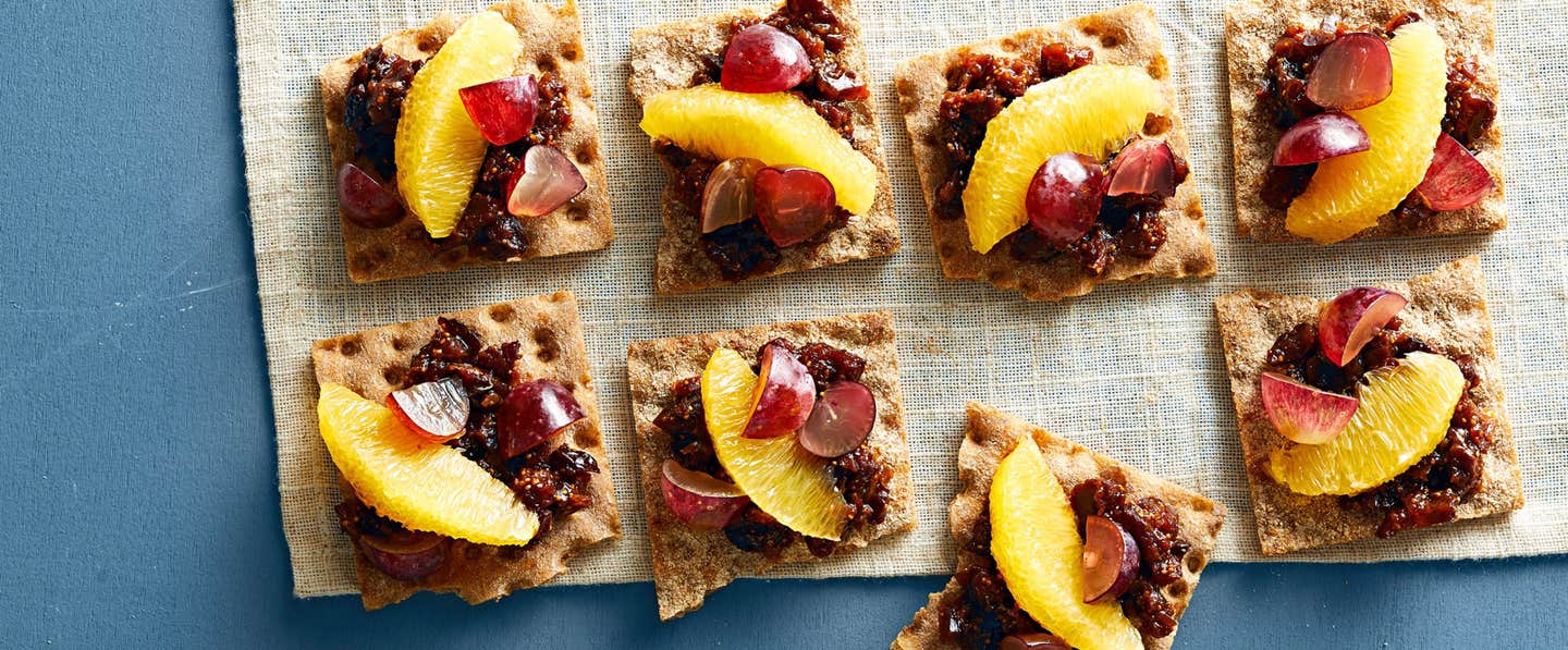 Four Grape and Fig Snacks on whole grain crackers, on a rough linen fabric on a blue table