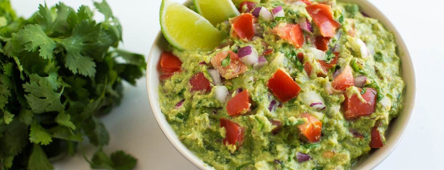 Not-So-Fat Guacamole with lime wedges in the bowl, next to a bunch of fresh cilantro