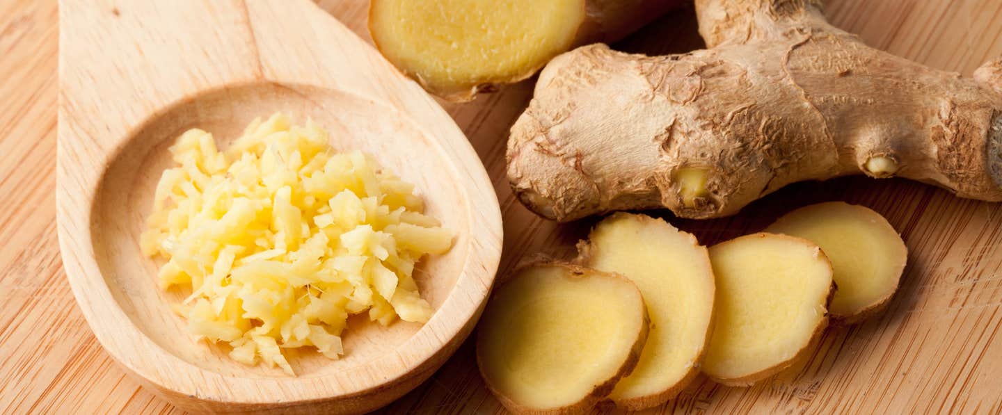 A whole root of fresh ginger next to slices of ginger and a wooden spoon of grated ginger