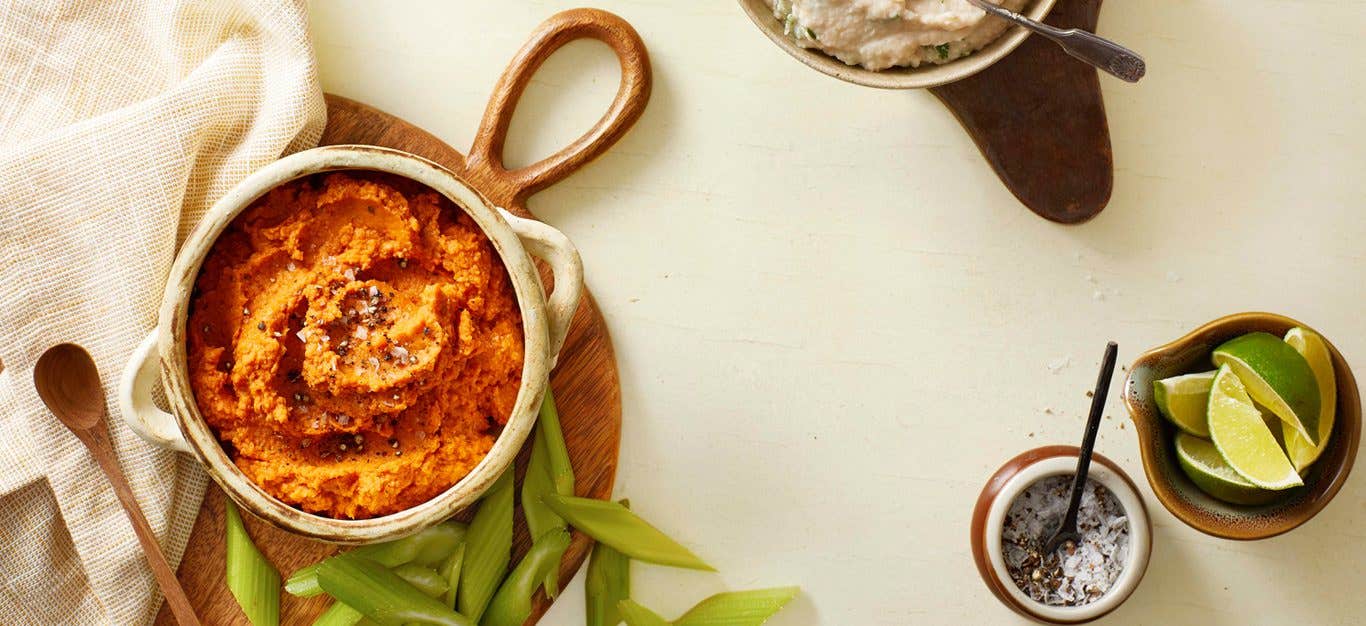 A table with a bowl of harissa roasted hummus, along with edamame and a ramekin of sliced limes