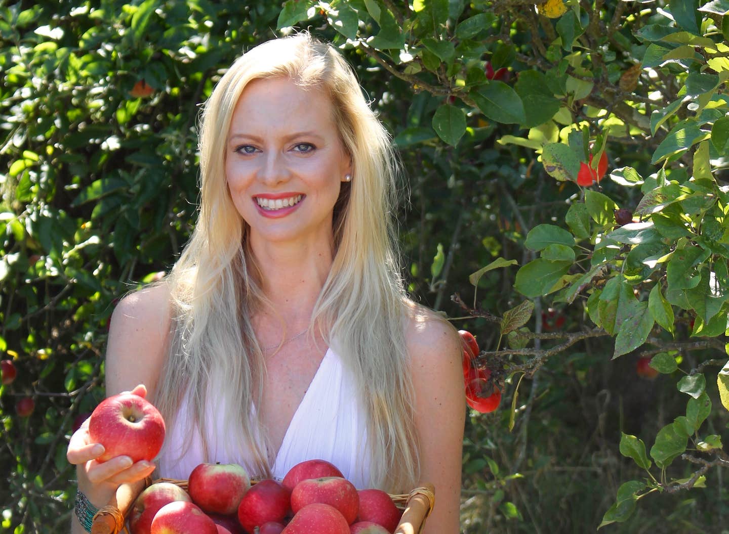 A smiling Lida van der Byl-Knoefel next to an apple tree holding a basket of apples