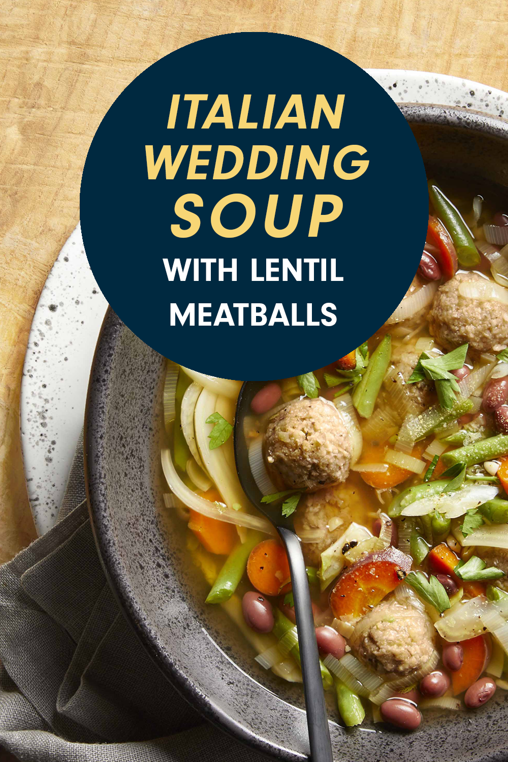 A veggie soup with vegan meatballs in a gray bowl against a wooden tabletop. Text reads, "Vegan Italian Wedding Soup."