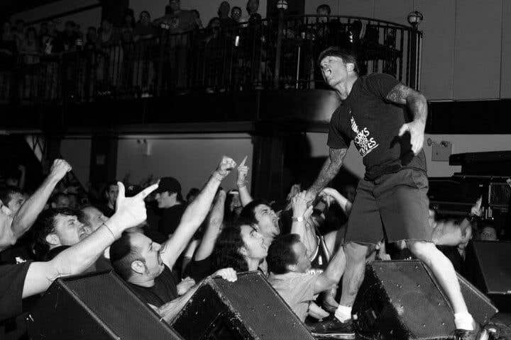 Black and white photo of John Joseph of the Cro-Mags on stage reaching down to audience