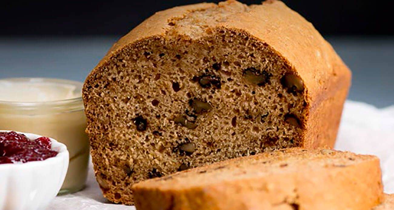 A loaf of Apple-Walnut Breakfast Bread with one slice cut next to a small dish of raspberry jam