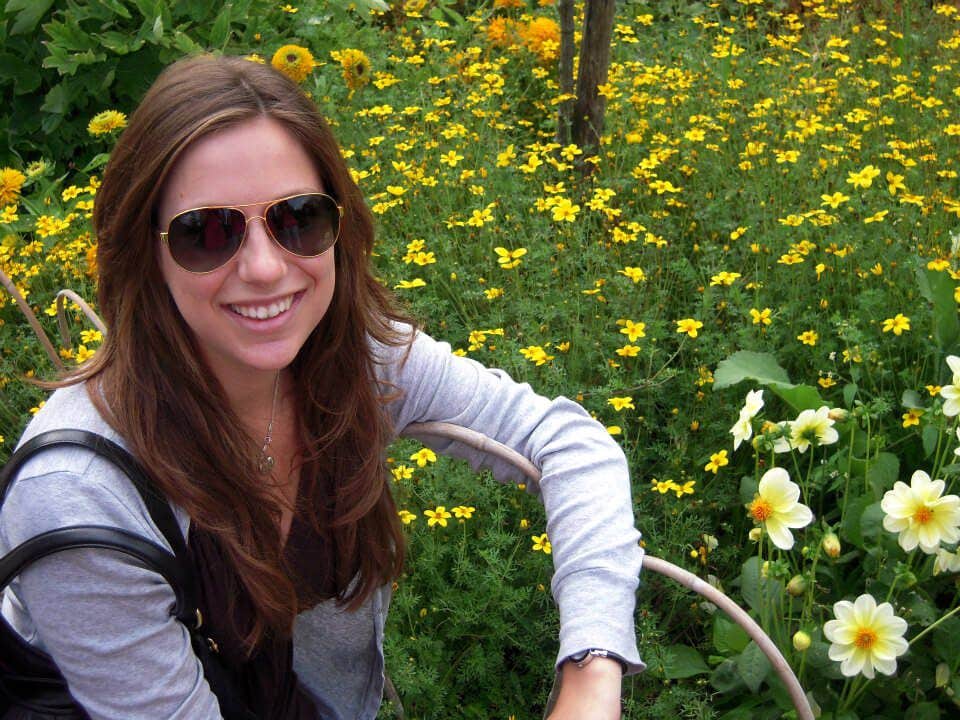 A happy Katie Behnke sitting in front of a field of yellow flowers