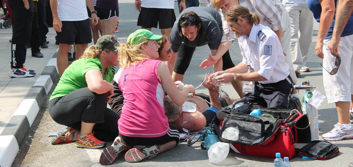 An EMS team surrounds a man lying on the ground having a cardiac arrest