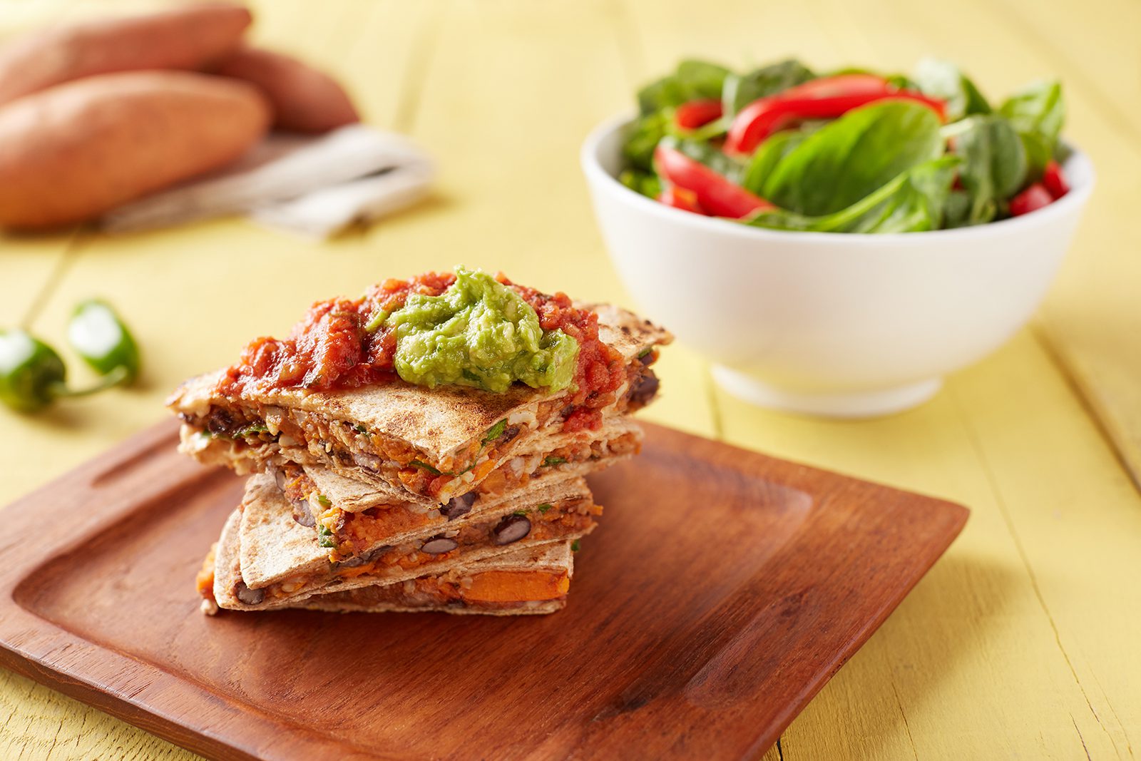 four stacked slices of black and sweet potato vegan quesadillas with guacamole on top