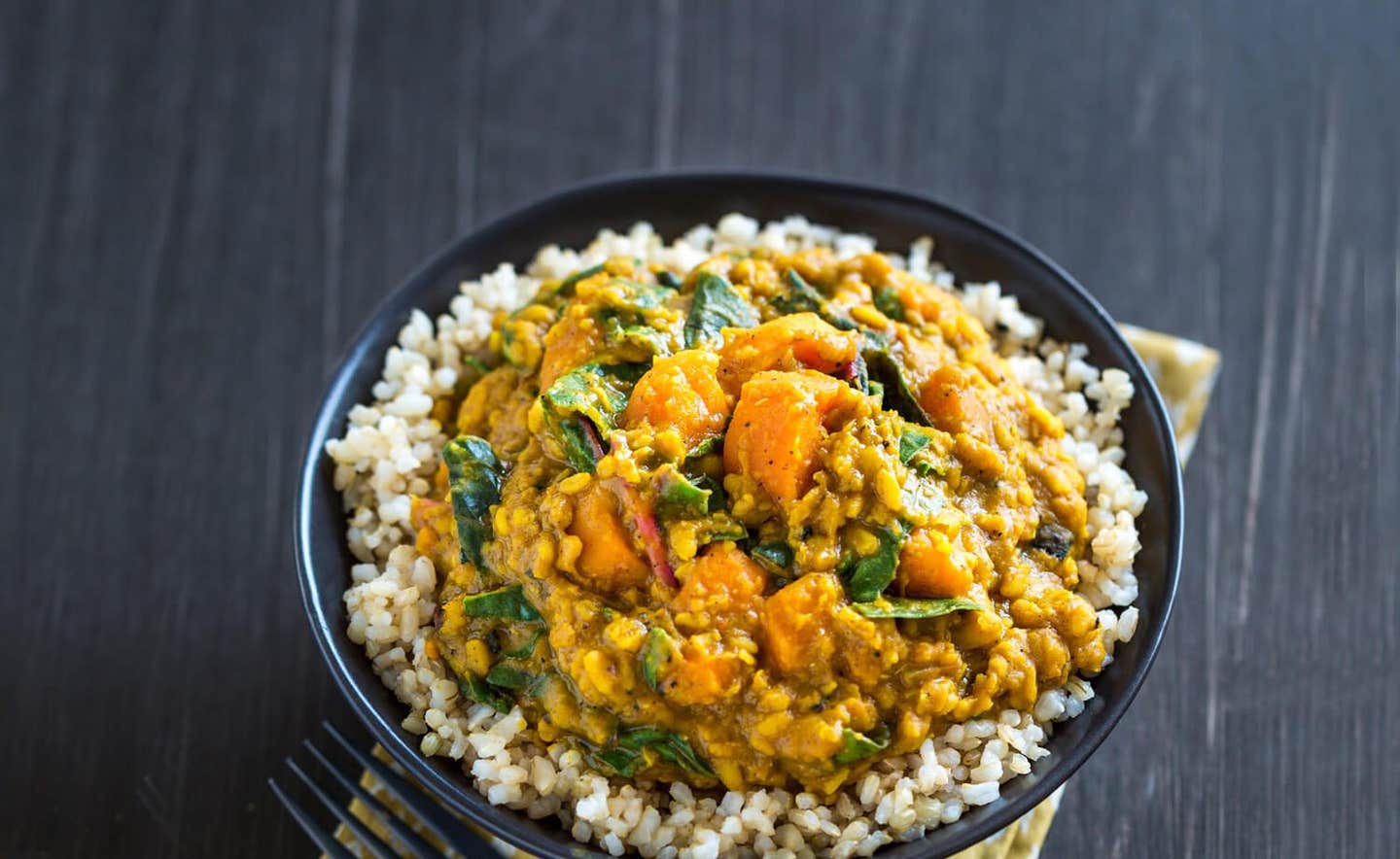 Lentil, Chard & Sweet Potato Curry atop brown rice in a black bowl