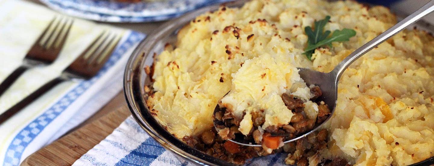 A casserole dish filled with Lentil Shepherd's Pie, with one spoonful being served up.