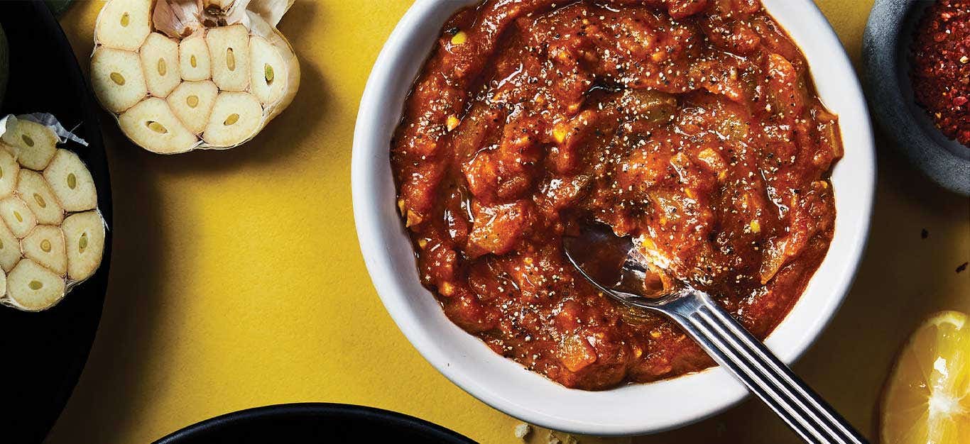 Masala Simmer Sauce in a white bowl next to halved heads of garlic