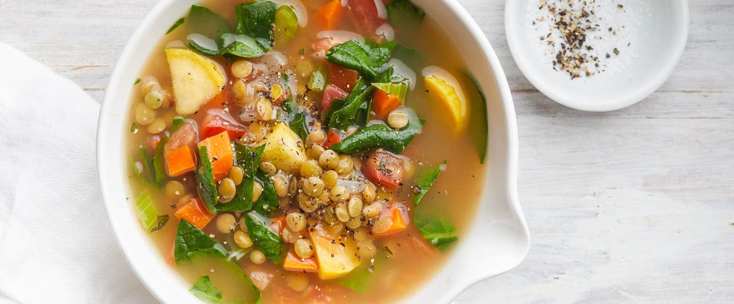 Mediterranean Lentil and Spinach Soup in a white bowl next to a pinch bowl of cracked black pepper