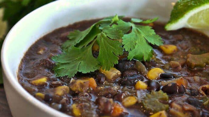 Mexican Black Bean Corn Soup in a white bowl with fresh cilantro and a lime wedge for a garnish