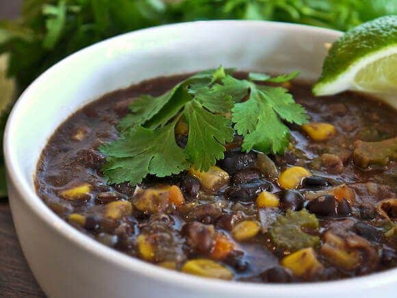 Mexican Black Bean Corn Soup in a white bowl with fresh cilantro and a lime wedge for a garnish