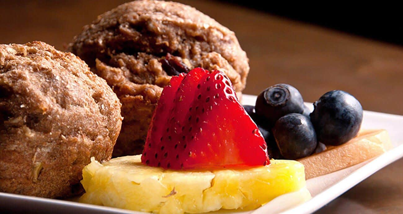 Two muffins on a plate with a disc of pineapple, fresh strawberries and blueberries, ready for Mother's Day