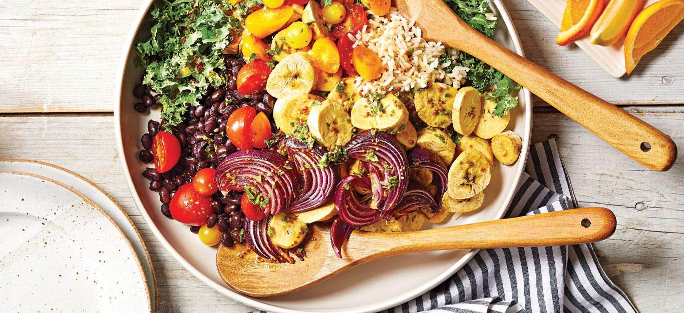 Mojo-Seasoned Plantain Salad with Black Beans and Rice in a white ceramic bowl with wooden serving spoons