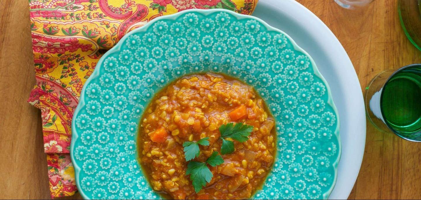 A top-down shot of Moroccan Lentil Soup in a turquoise bowl with a colorful red and yellow cloth napkin beside the bowl