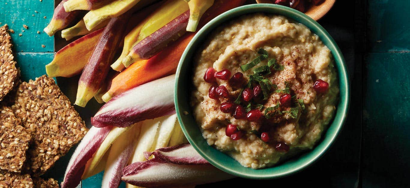 Moutabal (Eggplant Dip) in a turquoise bowl surrounded by carrots and endive