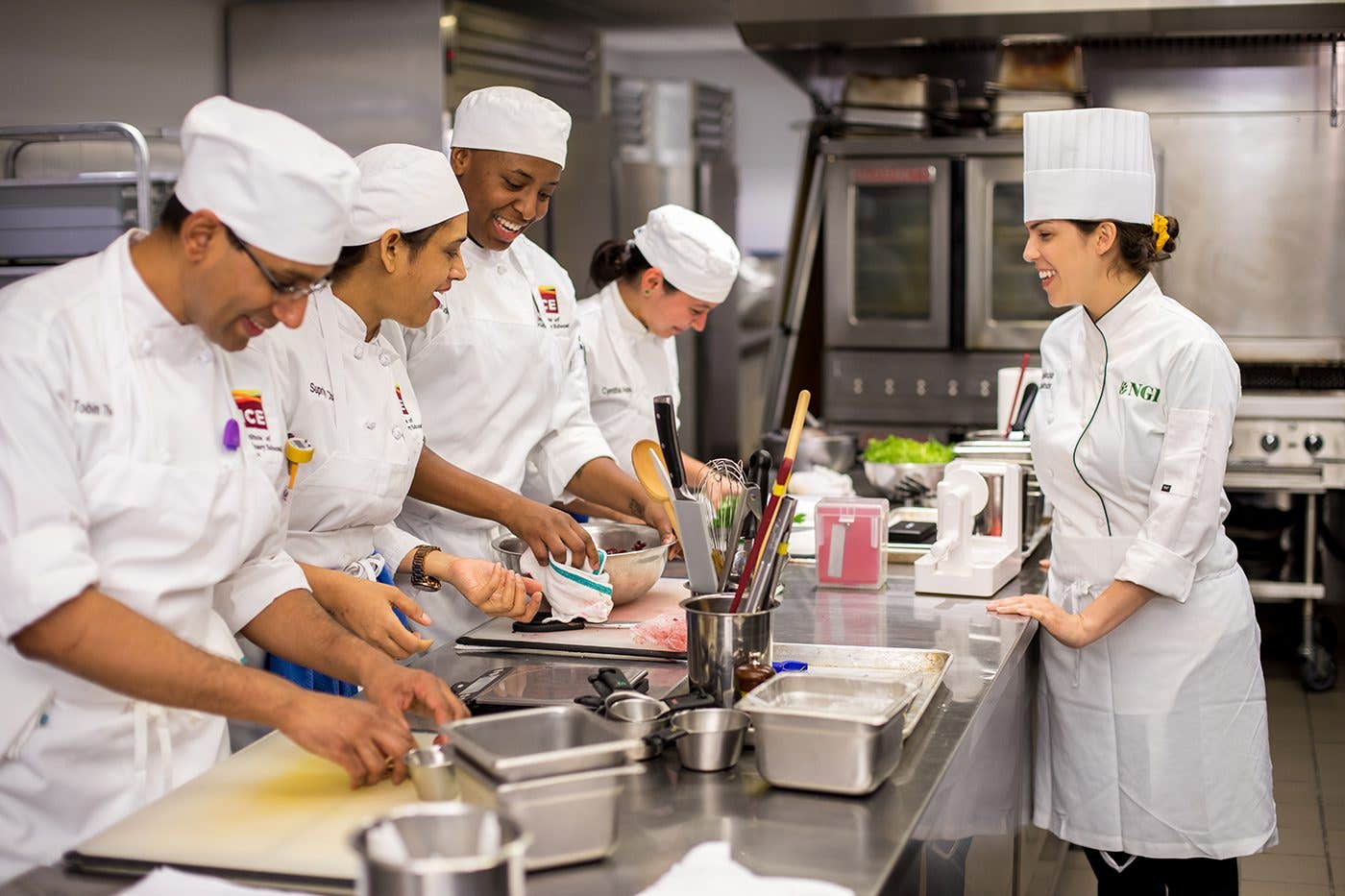 Chefs in white chef coats and hats smiled and laugh in a commercial kitchen