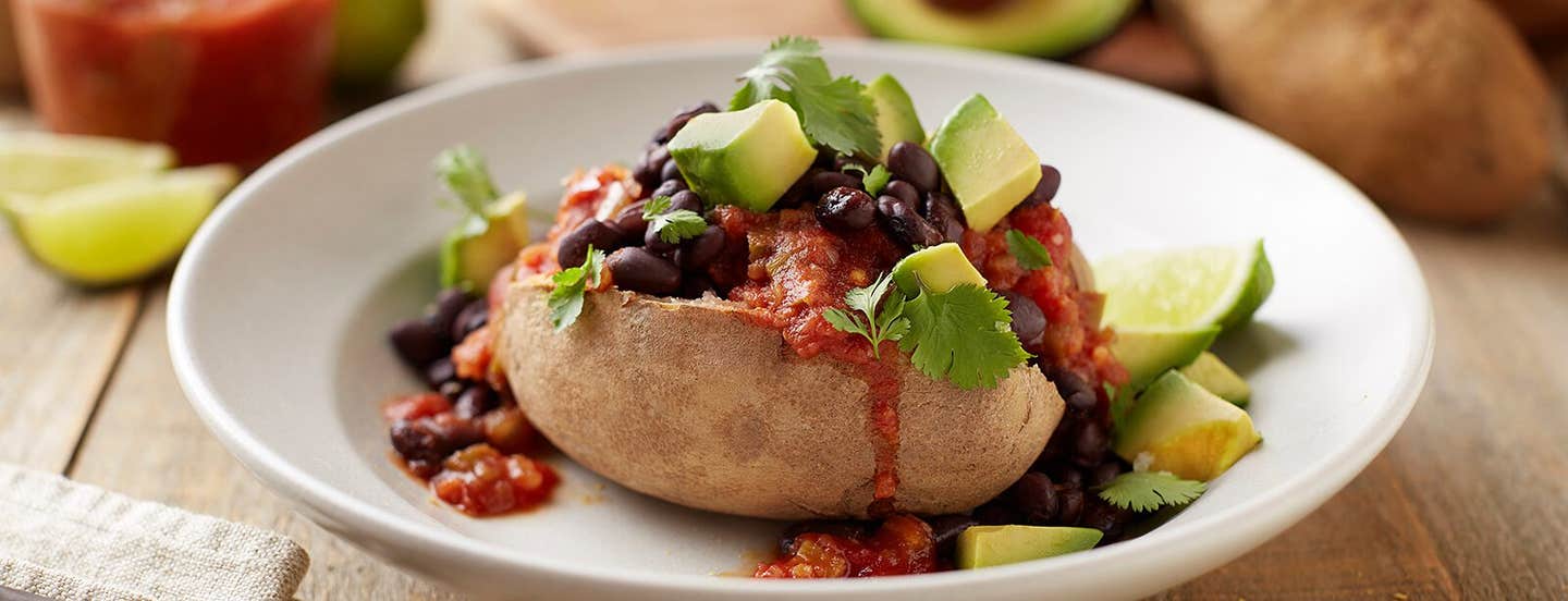 &quot;Nacho&quot; Vegan Baked Potato on a white plate with a garnish of slices of avocado and cilantro