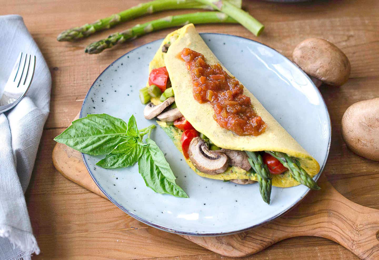 Leftover Veggie Chickpea Omelette topped with salsa on a blue plate with a sprig of basil