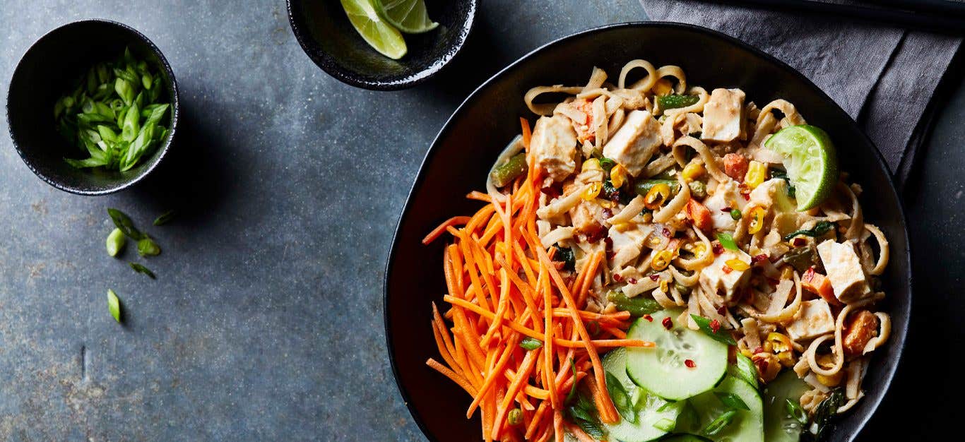 Pad Thai with Tofu sprinkeld with carrots and cucumbers in a large black bowl