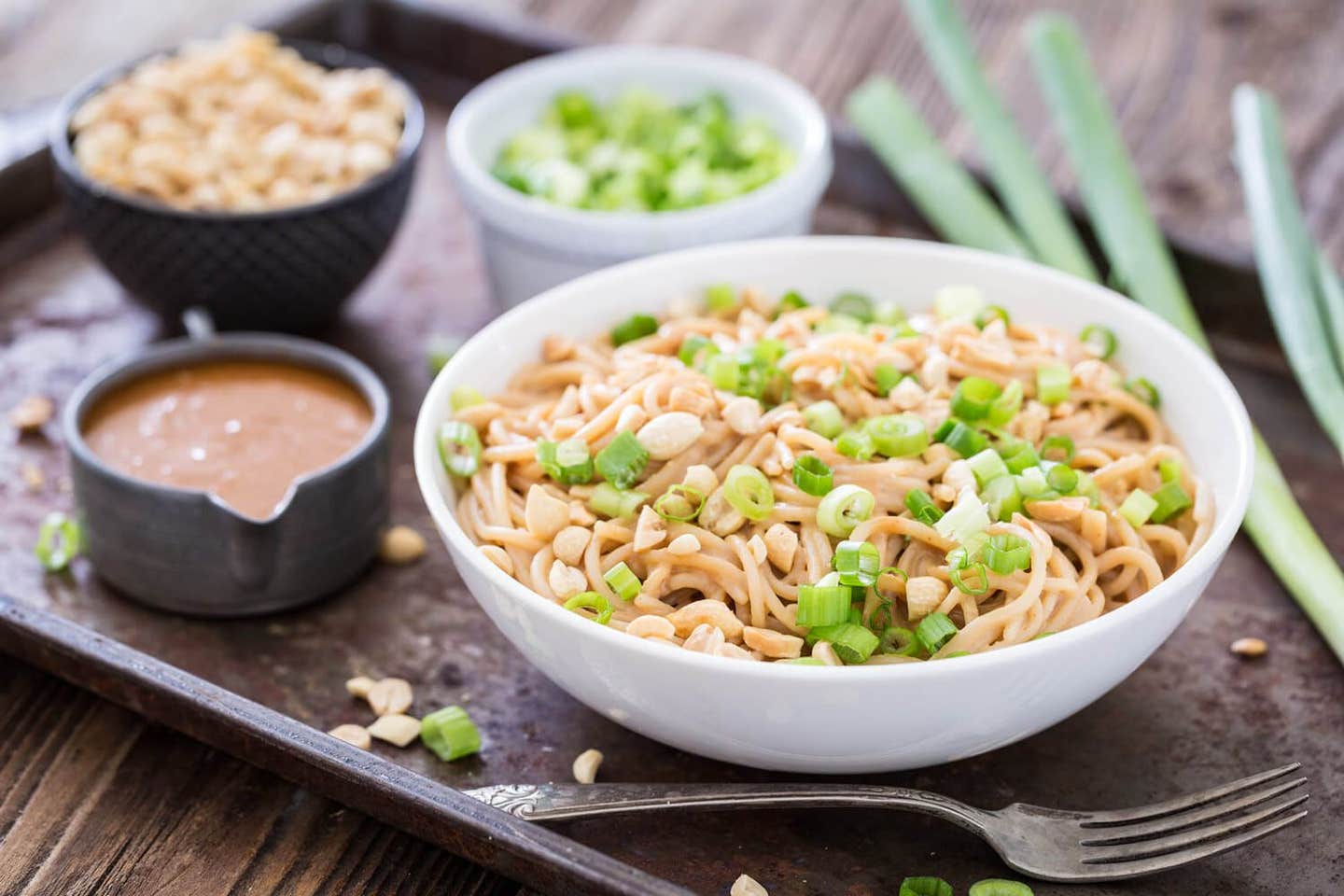 Chilled Peanut Noodles garnished with scallions and chopped peanuts, with small bowls of peanuts, scallions, and peanut sauce off to the side