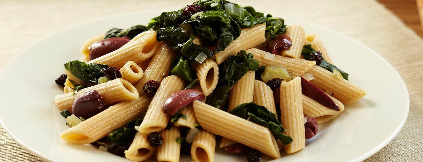 A white plate of Penne with Swiss Chard Olives and Currants