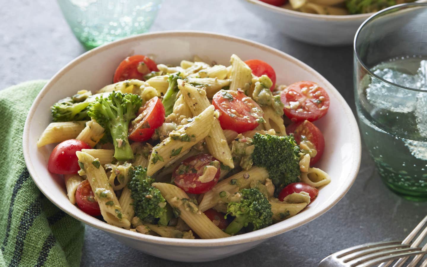 Pesto Penne in a white bowl next to a glass of water