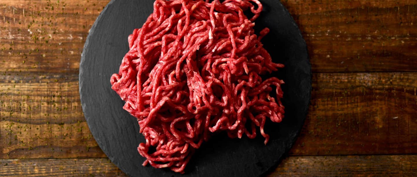 A pile of worm-like raw ground beef on a black plate