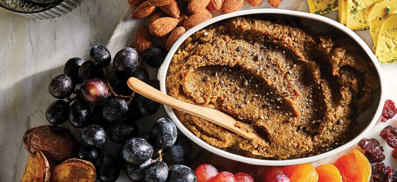 Porcini-Lentil Vegan Pâté in a white oval dish surrounded by fresh fruit and nuts