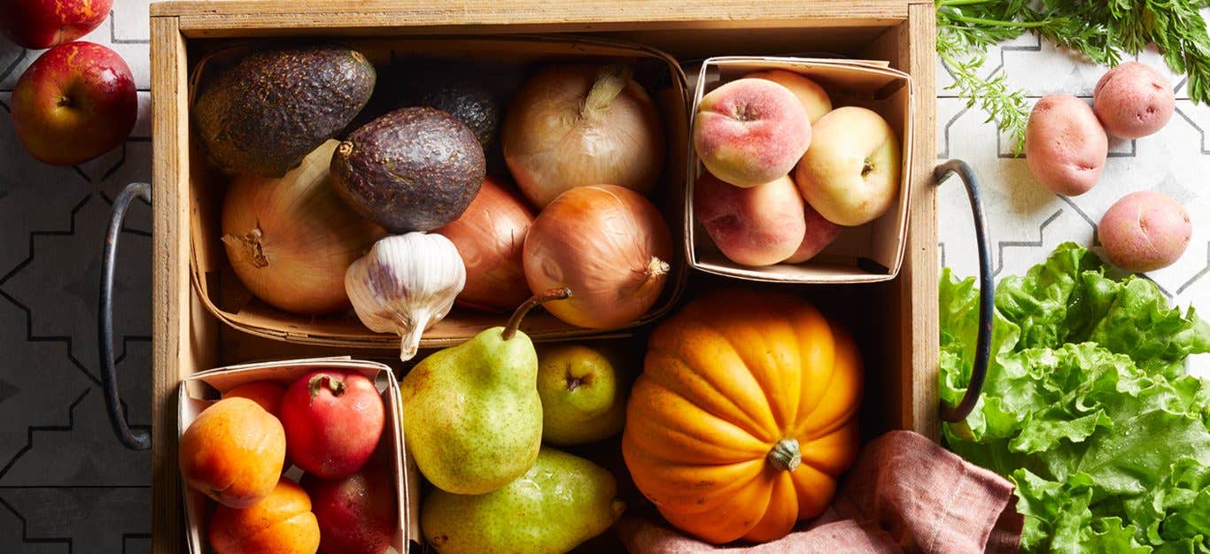 An assortment of fresh produce in a produce delivery box, including pumpkin, pears, peaches, potatoes