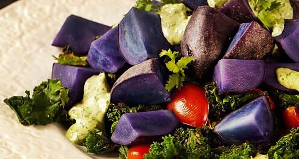 A closeup of part of a bowl of brightly colored Purple Potato and Kale Salad with Cilantro-Tahini Dressing