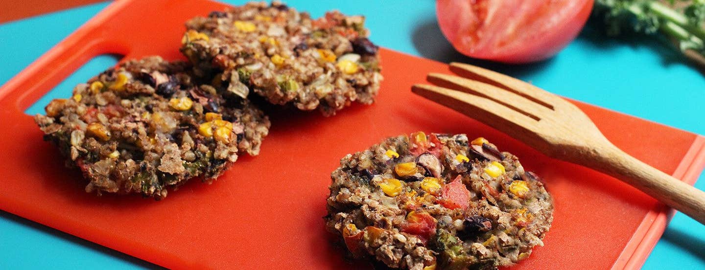 Three Plant-Based Rainbow Veggie patties on a red chopping board with a wooden serving fork