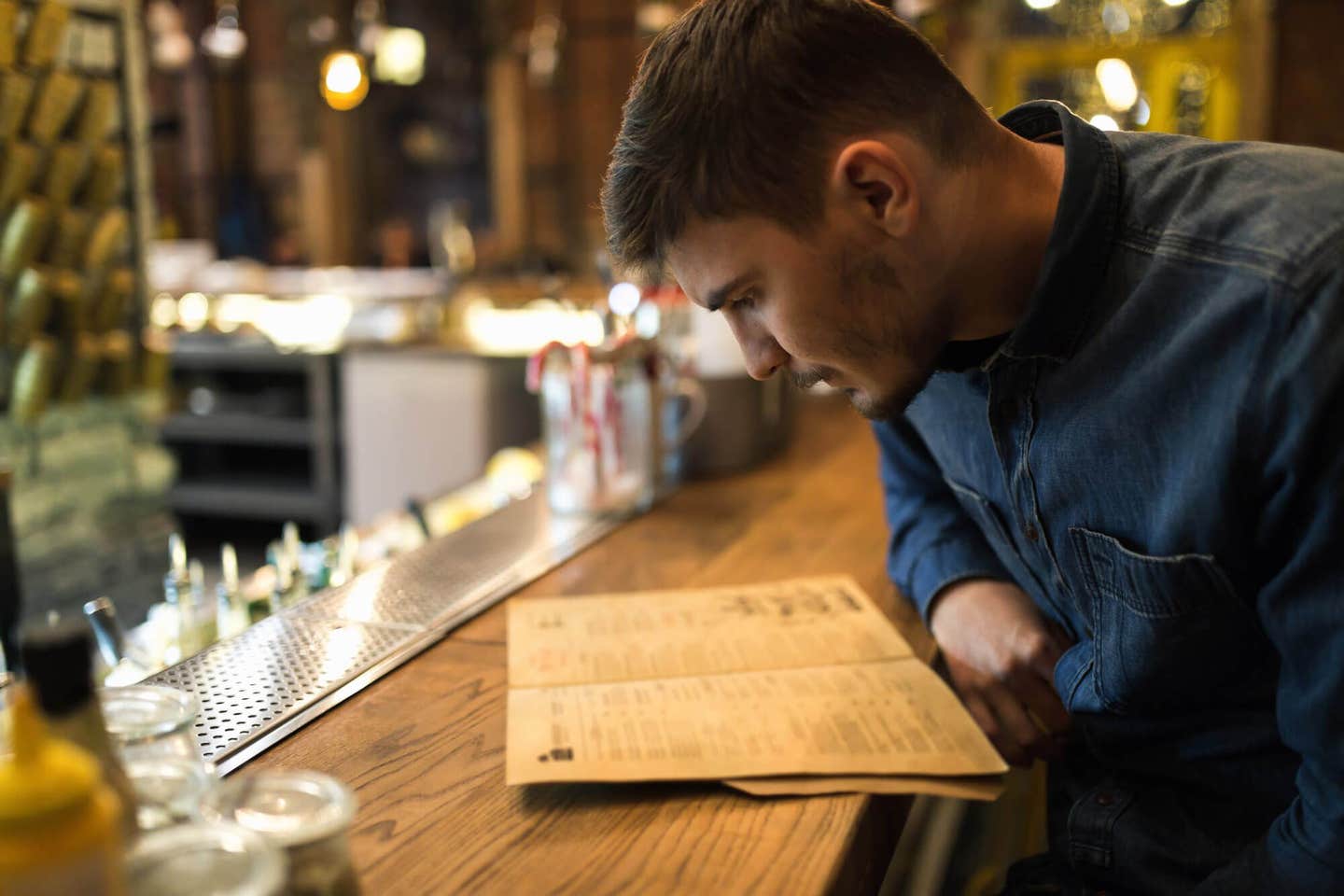 A young man sitting at a bar, looking intently at a dinner menu