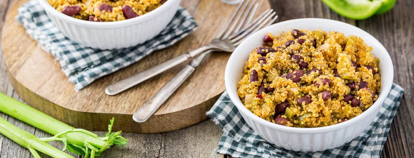 Two bowls of Red Beans and Quinoa. One bowl sits on a round wooden chopping board with a couple of forks; the other rests on a black-and-white checked napkin