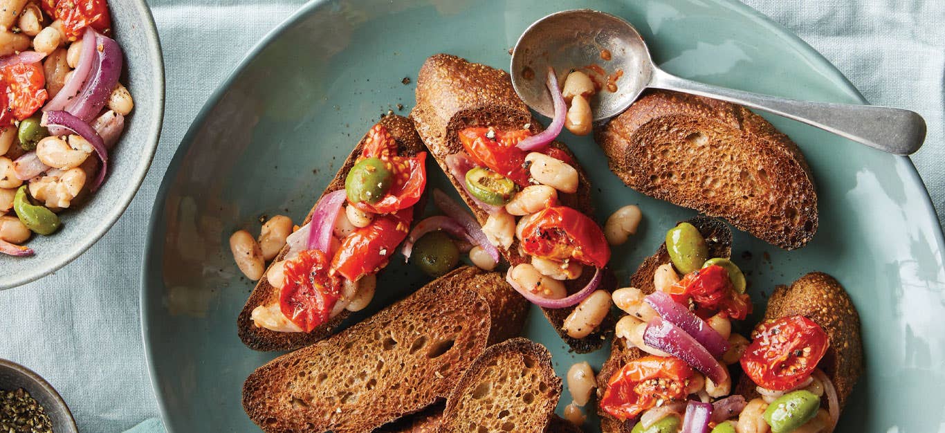 Roasted Tomato, White Bean, and Olive Bruschetta on a light blue ceramic plate