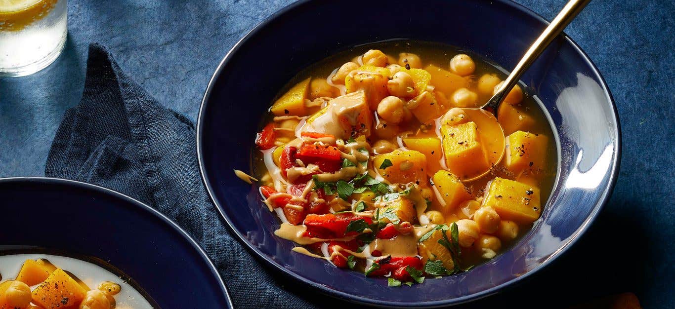 Roasted Red Pepper and Pumpkin Soup with Chickpeas in blue ceramic bowls with a metal soup spoon