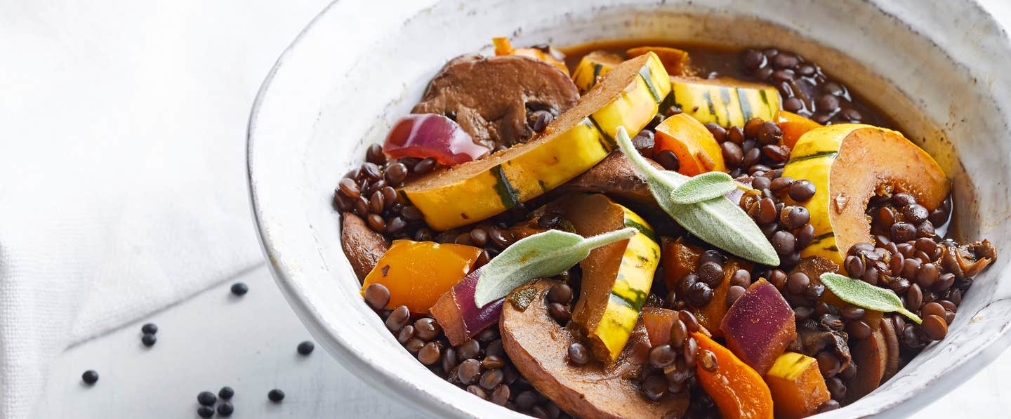 Sage Lentil Stew with Squash and Mushrooms in a rustic white bowl against a white background