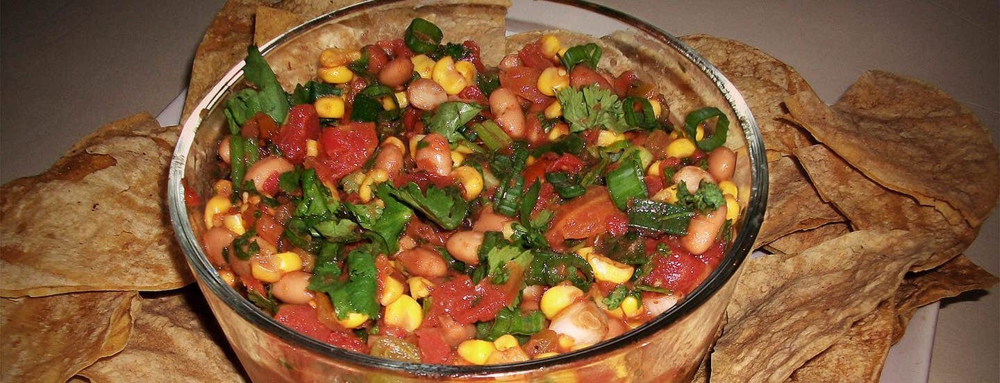 Chipotle Corn Salsa and Baked Tortilla Chips in a glass bowl with baked corn chips on a plate around the bowl