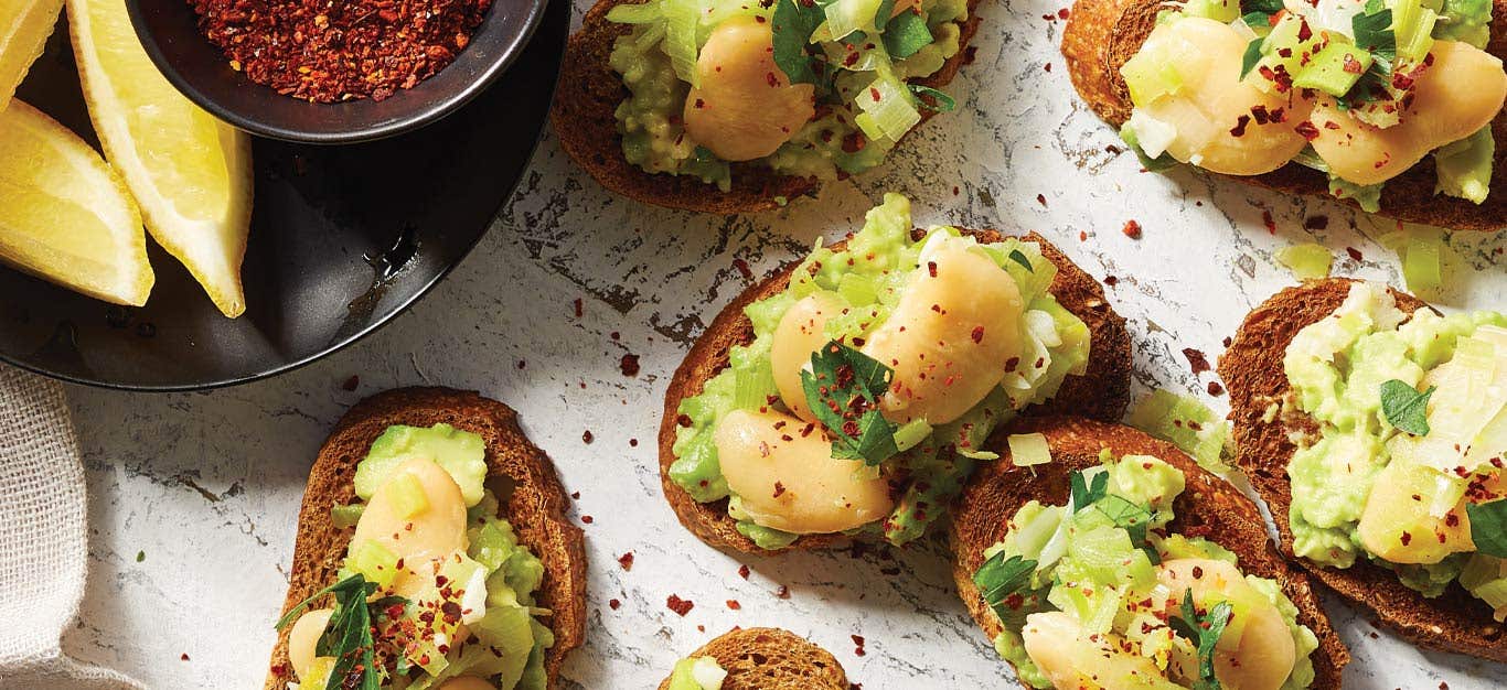 Sautéed Leek and Butter Bean Toasts on a white countertop next to lemon wedges and bowl of paprika