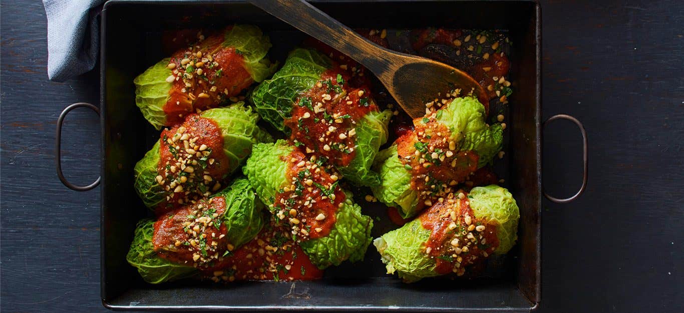 Savoy Cabbage Rolls in a casserole dish drizzled with tomato sauce and sprinkled with tomato sauce while a wooden spoon rests inside the dish