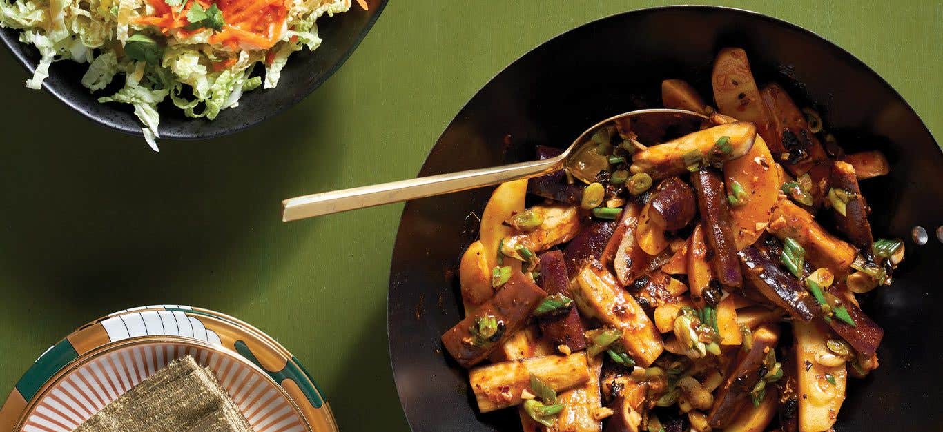 Sichuan Eggplant with Potatoes in a black bowl with a metal spoon against a green background